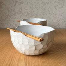 Load image into Gallery viewer, Two white ceramic bowls with a textured honeycomb pattern and light wood chopsticks resting on them, set on a wooden table against a gray textured wall.