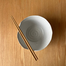 Load image into Gallery viewer, A speckled ceramic bowl with a spiral pattern inside, placed on a warm wood grain surface with a pair of wooden chopsticks resting across the rim.
